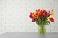 Vase with beautiful spring tulip flowers on table near brick wall. Royalty Free Stock Photo