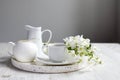 Vase with a blossoming branch of an apple tree. A set of white dishes: a cup of coffee, milk jug, a jug, a tray on the table Royalty Free Stock Photo