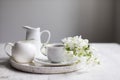 Vase with a blossoming branch of an apple tree. A set of white dishes: a cup of coffee, milk jug, a jug, a tray on the table Royalty Free Stock Photo