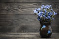 A vase with blue flowers stands on a wooden table. Wood texture. Royalty Free Stock Photo