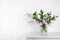 Vase with bouquet of beautiful flowers on table near brick wall Royalty Free Stock Photo