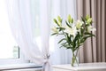 Vase with bouquet of beautiful lilies on white table indoors