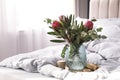 Vase with bouquet of beautiful Protea flowers on bed indoors