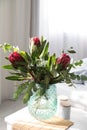 Vase with bouquet of beautiful Protea flowers on white table in bedroom