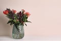Vase with bouquet of beautiful protea flowers on white wooden table near beige wall. Space for text