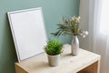 Vase and a bucket with green plants on a table near a picture with copy space. Place for text. Cozy interior