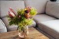 Vase with exotic protea flowers bouquet on coffee table with blurred background of modern cozy light living room with