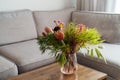 Vase with exotic protea flowers bouquet on coffee table with blurred background of modern cozy light living room with