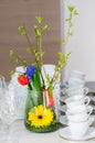 Vase with flowers on a buffet table with wineglasses and white cups