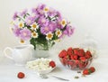 Vase of flowers, cottage cheese, ripe strawberry in a glass bowl on a white table. Still life