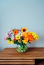 Vase with huge multicolor various mixed flower bouquet on the wooden sideboard with light gray wall background Royalty Free Stock Photo