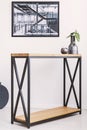 Vase with leaf and candle standing on stylish modern table with metal legs. Industrial poster on the wall