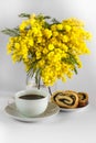 Vase with mimosa, cup of coffee and poppy seed strudel on a white background
