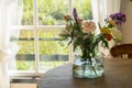 Vase with a mixed bouquet of flowers standing on a wooden table behind a window in the kitchen Royalty Free Stock Photo