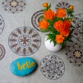 Vase with orange spring summer flowers Trollius asiaticus and blue stone with word hello on circle patterns background