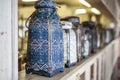 Vase in Oriental style with intricate ornament stands on a light wooden vintage shelf, in a row of many vintage vases, blurred