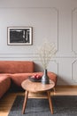 Flowers in vase and red fruits in bowl on wooden coffee table in elegant living room interior with ginger sofa