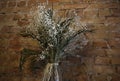 Vase with small white wild flowers at bricks wall background
