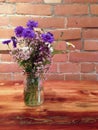 Vase of summer wildflowers on wooden table against brick wall