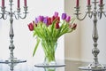 A vase of move tulips ona glass table with silver candlesticks