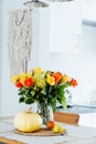 A vase of yellow and orange rose flowers, fresh pumpkin, apple and pear on a kitchen table counter with white modern Royalty Free Stock Photo