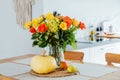 A vase of yellow and orange rose flowers, fresh pumpkin, apple and pear on a kitchen table counter with white modern Royalty Free Stock Photo