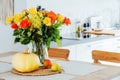 A vase of yellow and orange rose flowers, fresh pumpkin, apple and pear on a kitchen table counter with white modern Royalty Free Stock Photo