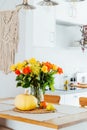 A vase of yellow and orange rose flowers, fresh pumpkin, apple and pear on a kitchen table counter with white modern Royalty Free Stock Photo