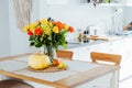 A vase of yellow and orange rose flowers, fresh pumpkin, apple and pear on a kitchen table counter with white modern Royalty Free Stock Photo