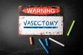 VASECTOMY. Metal warning sign and colored pieces of chalk on a dark chalkboard background