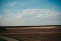 Vast empty field beneath a blue cloudy sky with trees and bushes in the distance Royalty Free Stock Photo