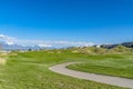 Vast grassy field with a curving paved road and houses beyond the slopes Royalty Free Stock Photo