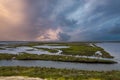 Vast miles of lush green marsh surrounded by deep blue ocean water with powerful clouds at sunset at Bolsa Chica Reserve