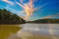 A vast rippling lake surrounded by lush green trees and bare winter trees on the banks with blue sky and powerful clouds Royalty Free Stock Photo