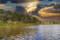 A vast rippling lake surrounded by lush green trees and bare winter trees on the banks with blue sky and powerful clouds Royalty Free Stock Photo