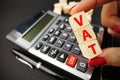 VAT calculation concept with woman hand holding vat word on wooden cubes above calculator keyboard on dark background