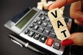 VAT calculation concept with woman hand holding vat word on wooden cubes above calculator keyboard on dark background