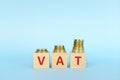 VAT letters on wooden blocks in blue background increasing stack of coins. Increase on value added tax Royalty Free Stock Photo
