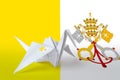 Vatican City State flag depicted on paper origami crane wing. Handmade arts concept