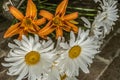 Orange lilies with decorative large daisies in a crystal vase on a brick wall