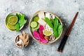 Vegan asian udon noodles soup bowl with ginger and mushrooms broth, tofu, snap peas, zucchini, watermelon radish and lime