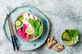 Vegan asian udon noodles soup bowl with ginger and mushrooms broth, tofu, snap peas, zucchini, watermelon radish and lime