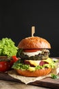 Vegan burger and vegetables on table against dark background.