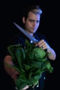 Vegan chef holds a bundle of raw spinach and a cleaver in his other hand with a ring, looking defiantly Royalty Free Stock Photo