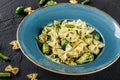 Vegan Farfalle pasta in a spinach sauce with broccoli, brussels sprouts, green beans in plate on dark stone background. Top view,