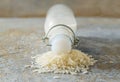 Vegan milk, front view of a capped bottle lying on a heap of rice grains on a rough stone background, alternative dairy product,