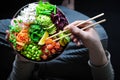 Vegan poke bowl with marinated watermelon, edamame, avocado, seaweed and carrot noodles. Man holding plate and chopstick