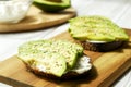 Vegan sandwich, rye bread toast, avocado, vegenaise eggless mayonnaise sauce, sesame seeds seasoning, white wood texture table. Ve