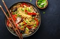 Vegan stir fry egg noodles with vegetables, paprika, mushrooms, chives and sesame seeds in bowl. Asian cuisine dish. Black table