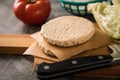 Vegan vegetarian burger patty raw on wooden cutting board and knife with iceberg lettuce and tomato on dark concrete background Royalty Free Stock Photo